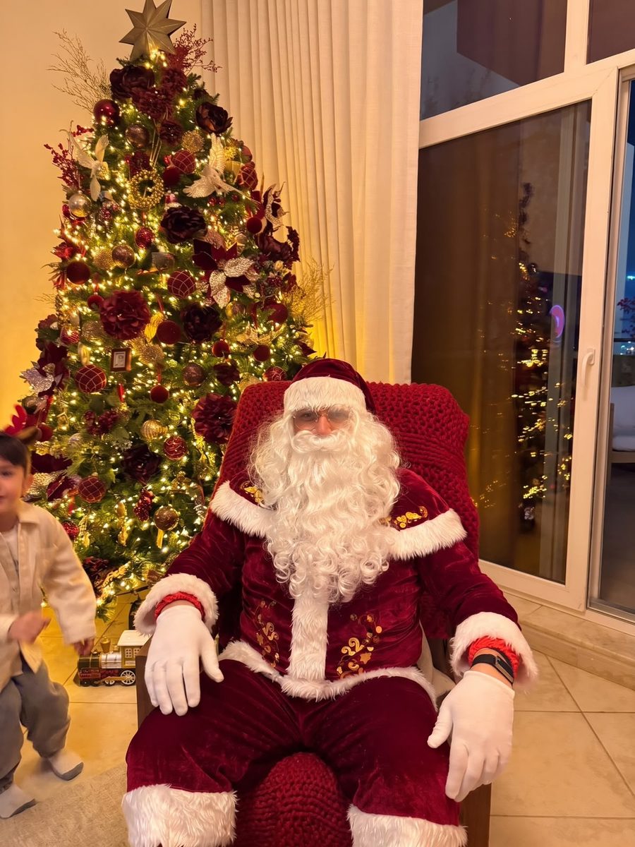 Santa in his red velvet suit, seated beside a glowing Christmas tree